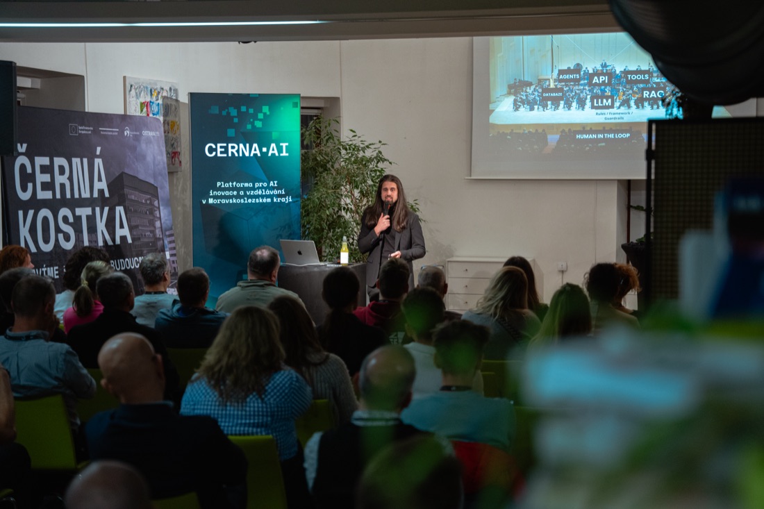 Audience at a ČERNÁ.AI event below the Černá kostka screens